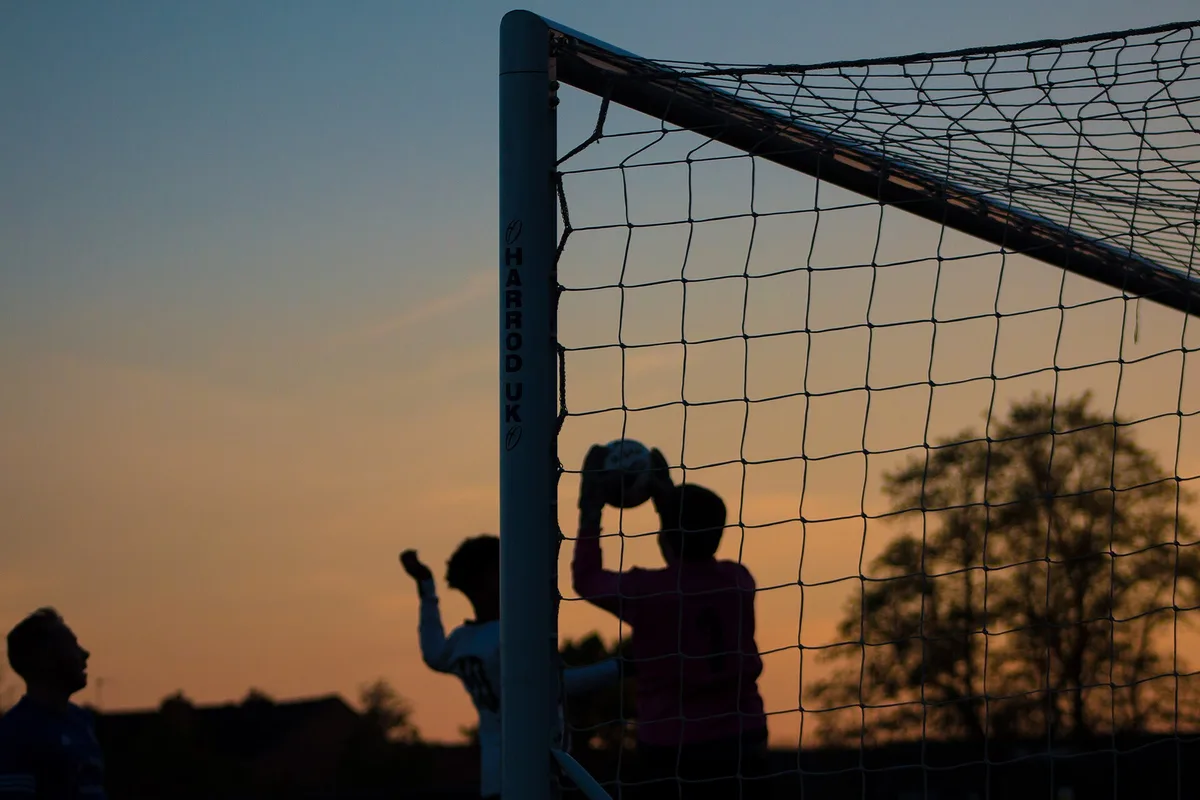 Silhouette of a soccer goalkeeper catching the ball in front of the net at sunset