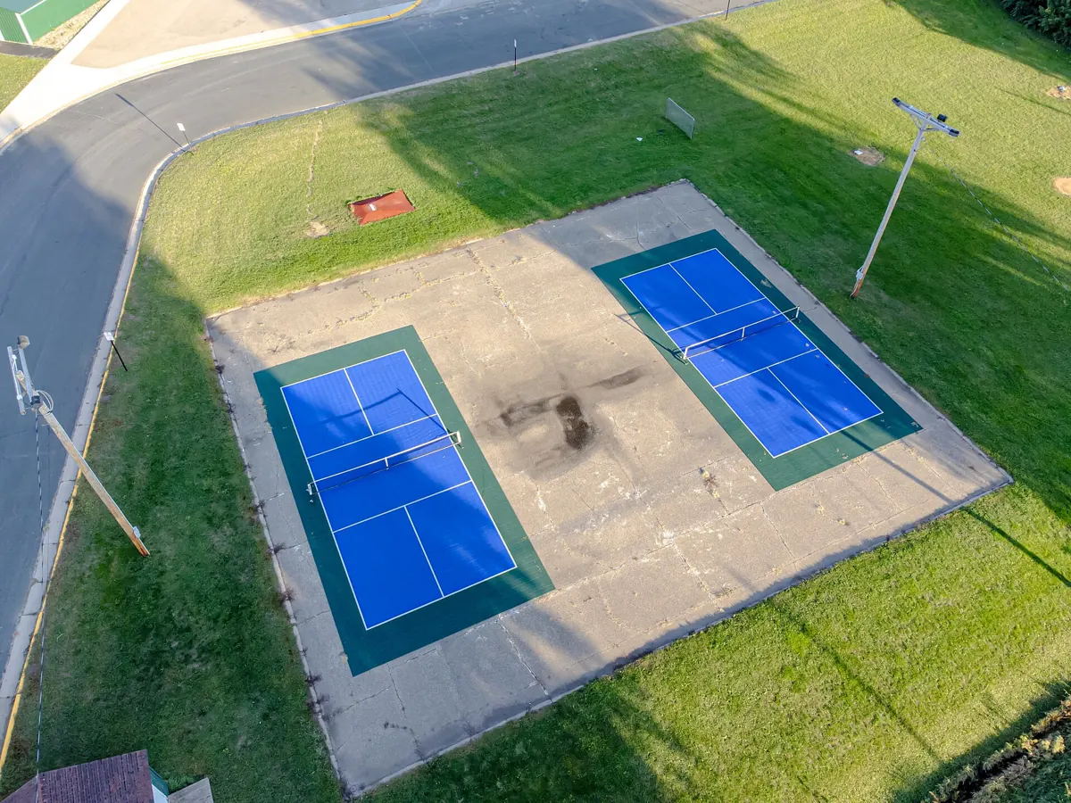 Aerial view of two blue outdoor pickleball courts surrounded by grass