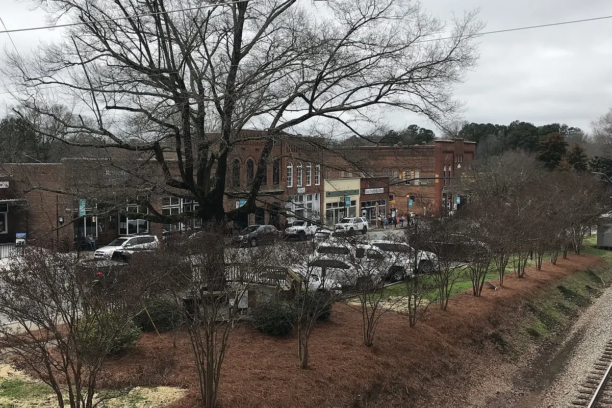 Brick storefronts in downtown Waxhaw behind bare winter trees beside the railroad tracks